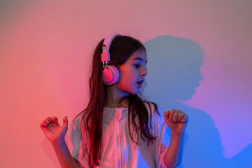 Portrait of a dancing happy little girl in pink headphones