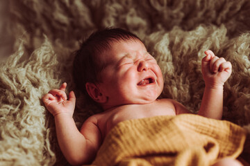 Cute baby lying on fur blanket and crying