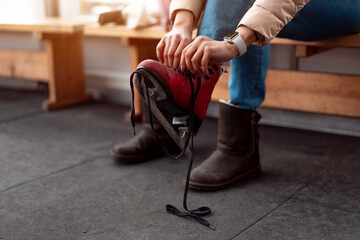 Winter time. Middle age woman put on ice skates sitting bench near ice skate rink.