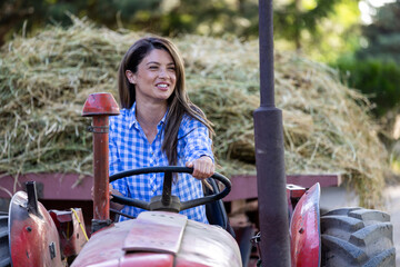 Woman driving tractor with hay in trailer on farm