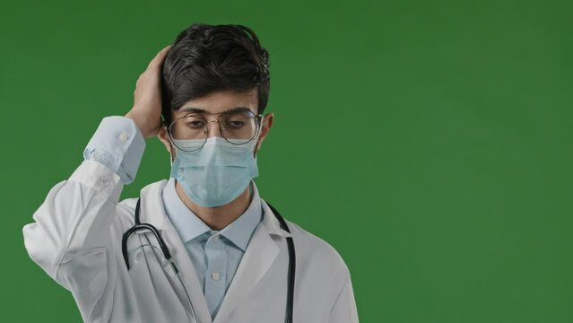 Portrait of upset hispanic young frustrated man therapist indian guy put hands on forehead tired overwhelmed doctor in mask cover face failure outrage bad news feel nervous stand on green background