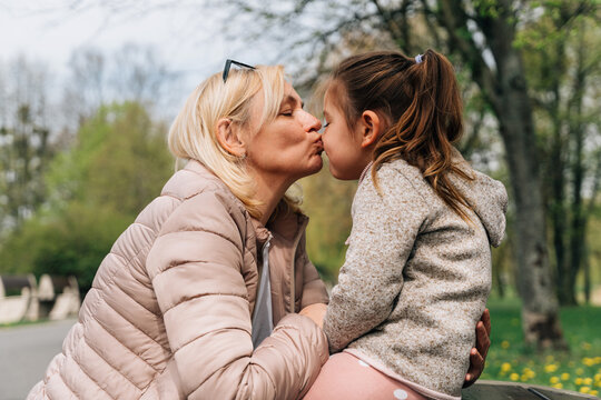 Mature grandma kissing nose of cute girl in park