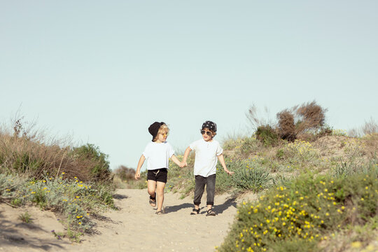 Happy little siblings holding hands while strolling on beach
