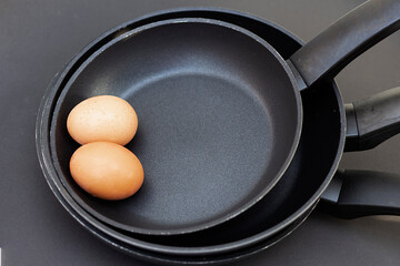 Set de tres sartenes de teflón con dos huevos , todo sobre fondo negro