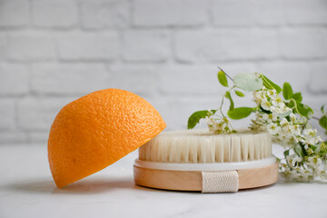 Massage brush, orange fruit, flower on a light background
