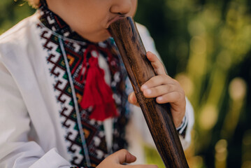 Adorable boy playing on woodwind wooden flute - ukrainian sopilka. Folk music concept. Musical...
