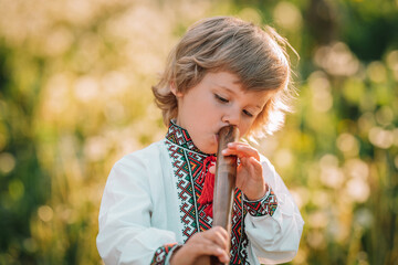 Adorable boy playing on woodwind wooden flute - ukrainian sopilka. Folk music concept. Musical...
