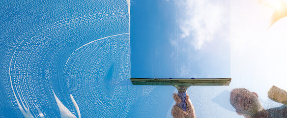 Window cleaner cleaning window with squeegee and wiper on a sunny day with a bright blue sky