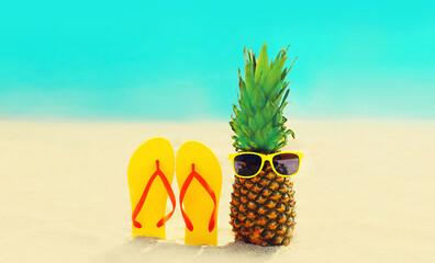 Summer vacation concept - pineapple with sunglasses and colorful flip flops on the beach on sea...