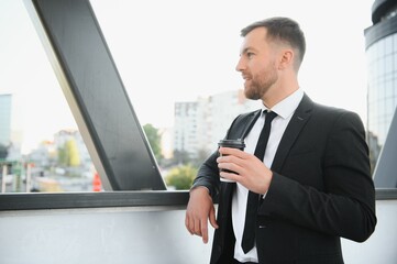 Fototapeta premium Close up serious businessman drinking take away coffee at street. Portrait of business man waiting with coffee to go outdoor. Office employee looking away at street. Male professional take break