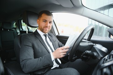 Man of style and status. Handsome young man in full suit smiling while driving a car