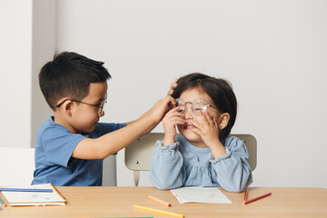 cute little kids are sitting together at the table and the boy is adjusting the girl's glasses