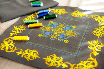 Cushion cover with beautiful, chic embroidery in yellow. On top are spools of thread in the same color scheme.