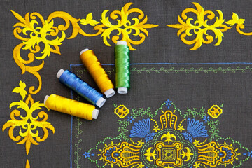Cushion cover with beautiful, chic embroidery in yellow. On top are spools of thread in the same color scheme.