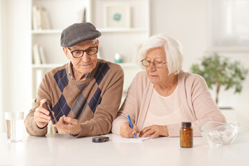 Elderly man and woman sitting at home with medications on a table and checking blood sugar