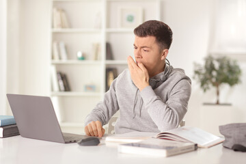 Guy sitting in front of a laptop computer at home and yawning