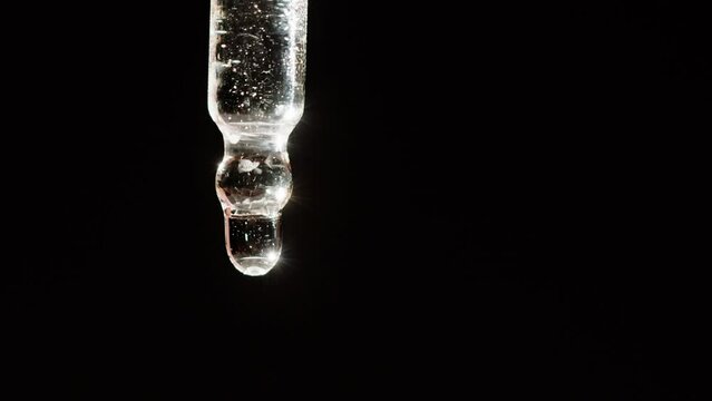 Dripping oil from pipette close-up, plant juice. Using aroma serum on black background. Dropping liquid extract, skincare routine, treatment essence oil, spa concept. Traditional medicine