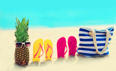Summer vacation concept - bag with pineapple and flip flops on the beach on blue sea background