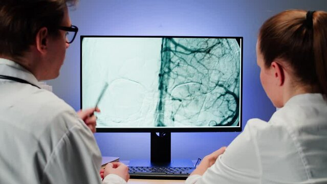 Doctors examining blood vessels X-ray on computer monitor. Magnetic resonance image of head. Therapist man and woman looking at human brain MRI close-up. Advanced research of body, checkup