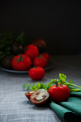 a cut tomato with herbs in the foreground and a plate of tomatoes in the background