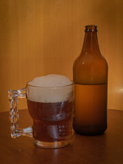 Large beer frozen mug with beer and white foam and opened bottle with beer on a wooden table and wood background top side view