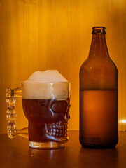 Large beer frozen mug with beer and white foam and opened bottle with beer on a wooden table and wood background