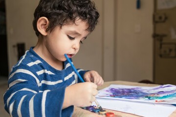 child painting with paints and colored pencil making a drawing