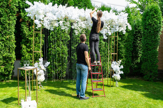 Woman and man decorate the wedding photo area with white flowers on a green lawn