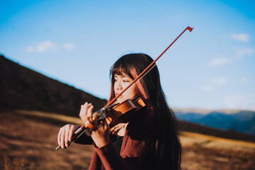 Detalle de Mujer joven tocando violín en una montaña al atardecer. Concepto de personas y música. - obrazy, fototapety, plakaty