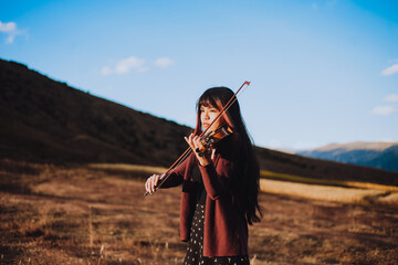 Mujer joven tocando violin en una montaña al atardecer. Concepto de personas y musica.