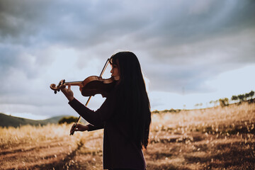 Silueta de Mujer joven tocando violin en una montaña al atardecer. Concepto de personas y musica.
