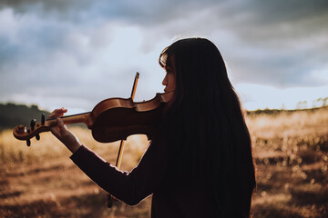 Silueta de Mujer joven tocando violin en una montaña al atardecer. Concepto de personas y musica. © artrolopzimages
