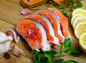 Raw salmon steaks lying on wooden table with herbs, vegetables and lemon. Cooking ingredients