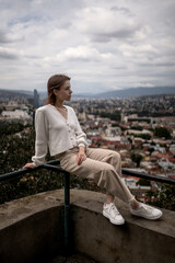Fototapeta na wymiar Stylish woman in a white sweater and beige pants is posing on the background of the city.