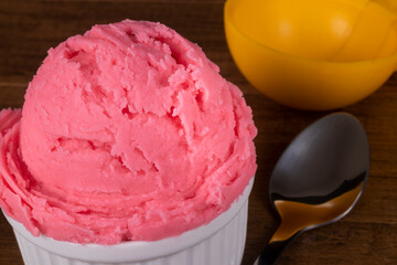 Strawberry Ice Cream served in the white pot with dessert spoon on the side and yellow ice cream spoon. Gastronomic photography close-up ice cream parlors and gelaterias.