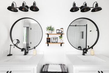 A modern farmhouse bathroom with a white vanity and marble countertop, circular black mirrors, and...