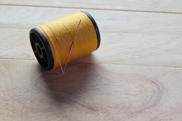 Yellow thread spool and sewing needle with copy space isolated on wooden background closeup.