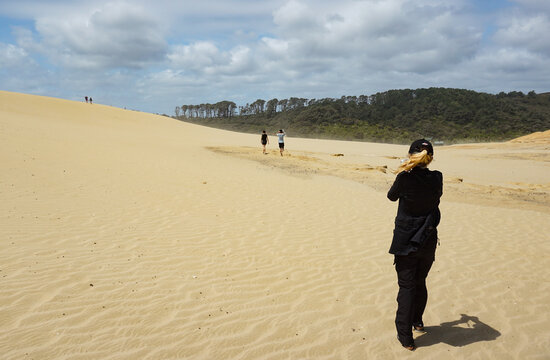 A woman walking and taking pictures at Great Sand Dune in Cape Reinga, Northland, New Zealand.