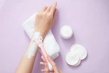 Top view of using razor to remove cream on hand with towel and cotton pad in purple background 