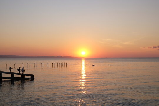 Sunset At The Beach With Silhouette Of Kids At The Pier About To Jump To Swim.