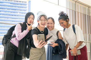 Group of young happy Asian women with diverse ethnicity laughing having fun while taking selfie with a smartphone.