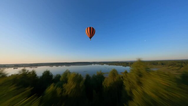 drone manoeuvres up and down around Black and orange hot air balloons above lake