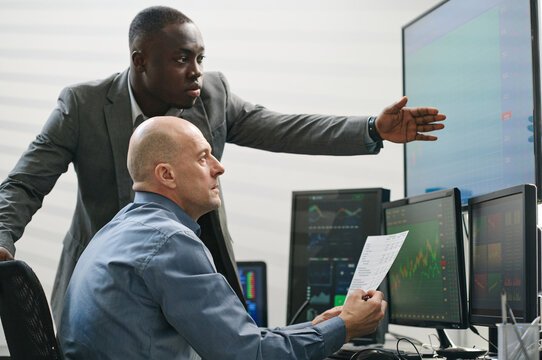 Two ethnically diverse stock trading specialists working with data looking at monitor screen and analyzing future results