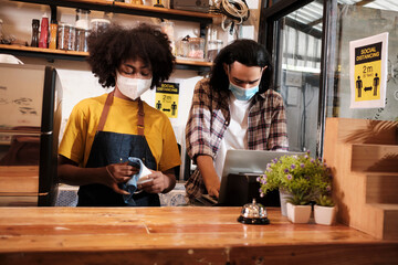 Two young cafe barista partners and entrepreneurs in aprons work with face masks in a coffee shop, service startup jobs in a new normal lifestyle, SME business impact from COVID19 pandemic quarantine.