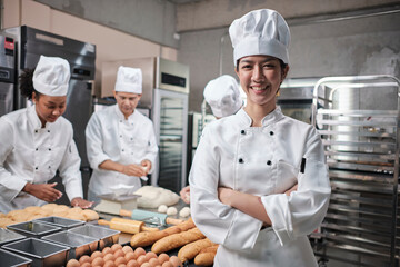 Young beautiful Asian female chef in white cooking uniform looks at camera, arms crossed and...