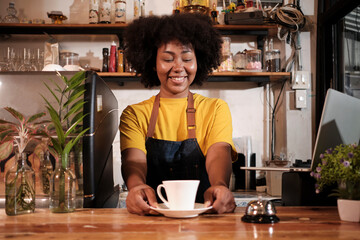 Fototapeta na wymiar African American female barista offers cup of coffee to customer with cheerful smile, happy service works in casual restaurant cafe, young small business startup entrepreneur.