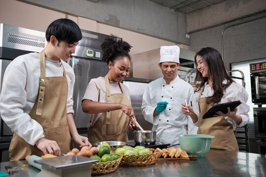 Hobby cuisine course, senior male chef in cook uniform teaches young cooking class students to prepare, mix and stir ingredients for pastry foods, fruit pies in restaurant stainless steel kitchen.