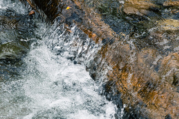 Turbulent spring stream of mountain river. Water foams, breaks into splashes on stones. Power of nature, continuous movement and energy.