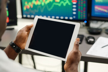 Close-up shot of unrecognizable man working on digital tablet in modern brokerage agency office, blank black screen, copy space