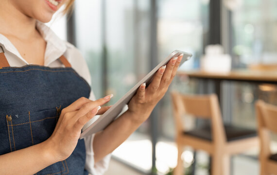 Asian woman barista holding digital tablet for checking order from customer at coffee cafe shop background , SME business concept